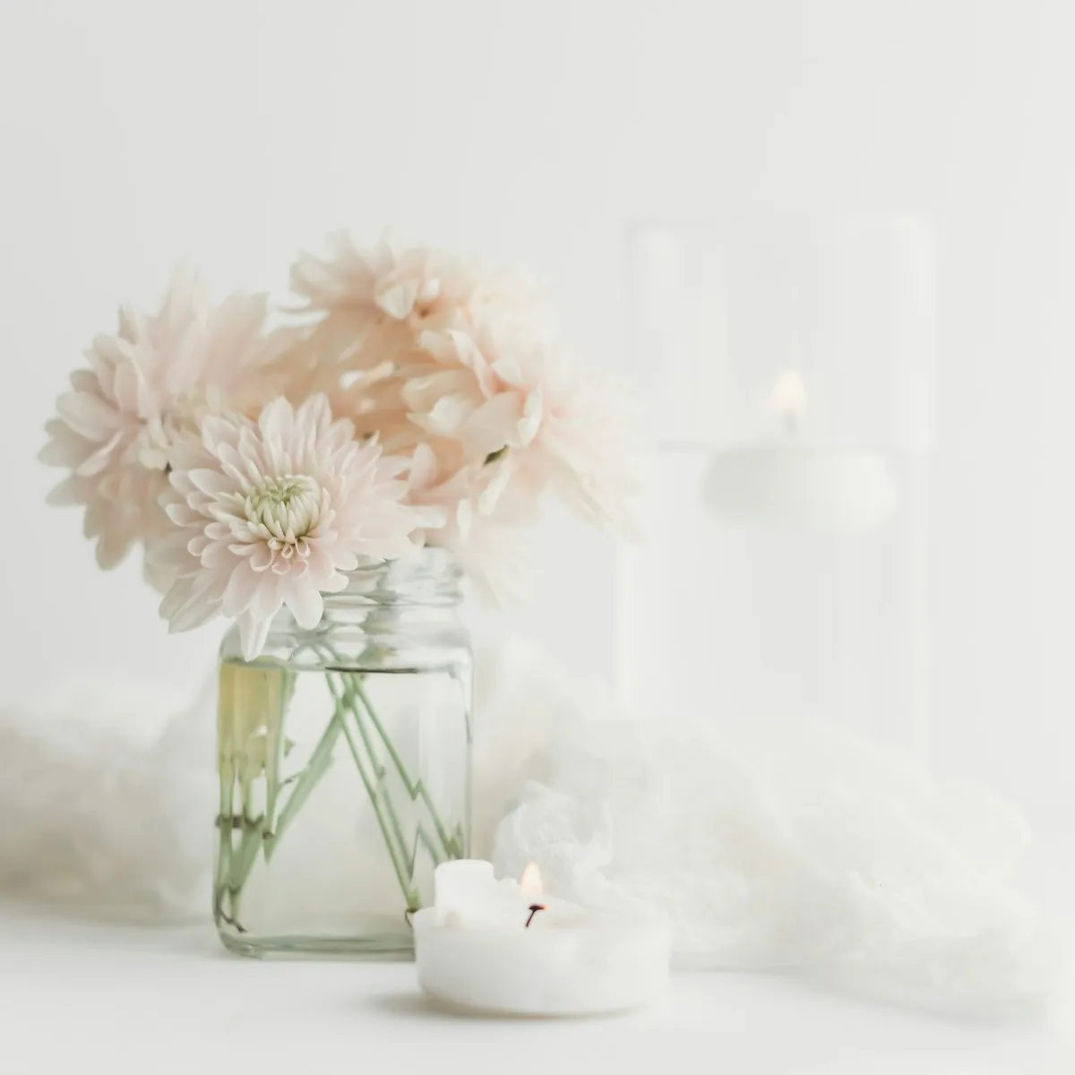 A glass vase of soft pink flowers beside a lit candle